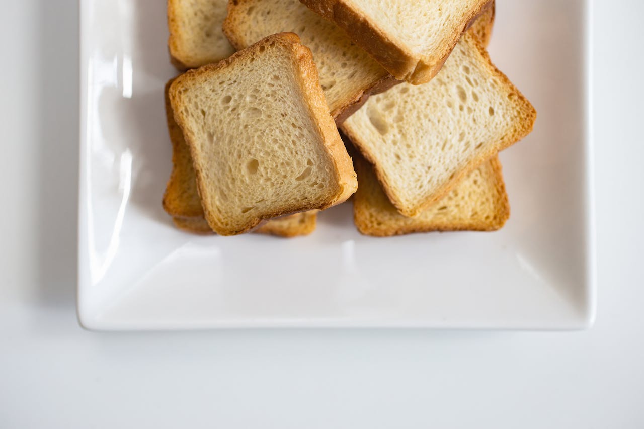 heros-img Stack of toasted bread slices on a white ceramic plate, perfect for breakfast or snacks.
